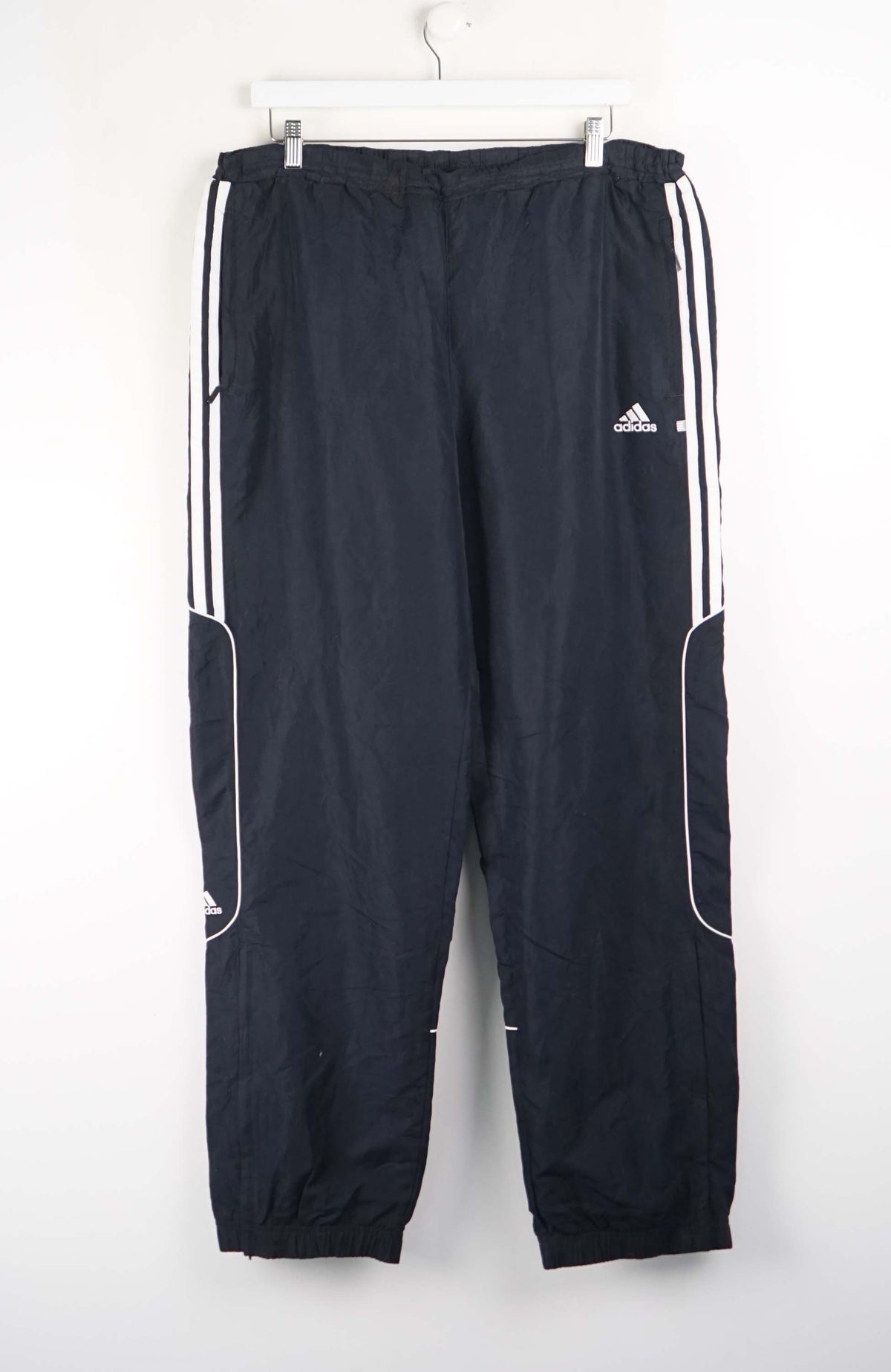 Black Adidas tracksuit pants with white stripes on a white background