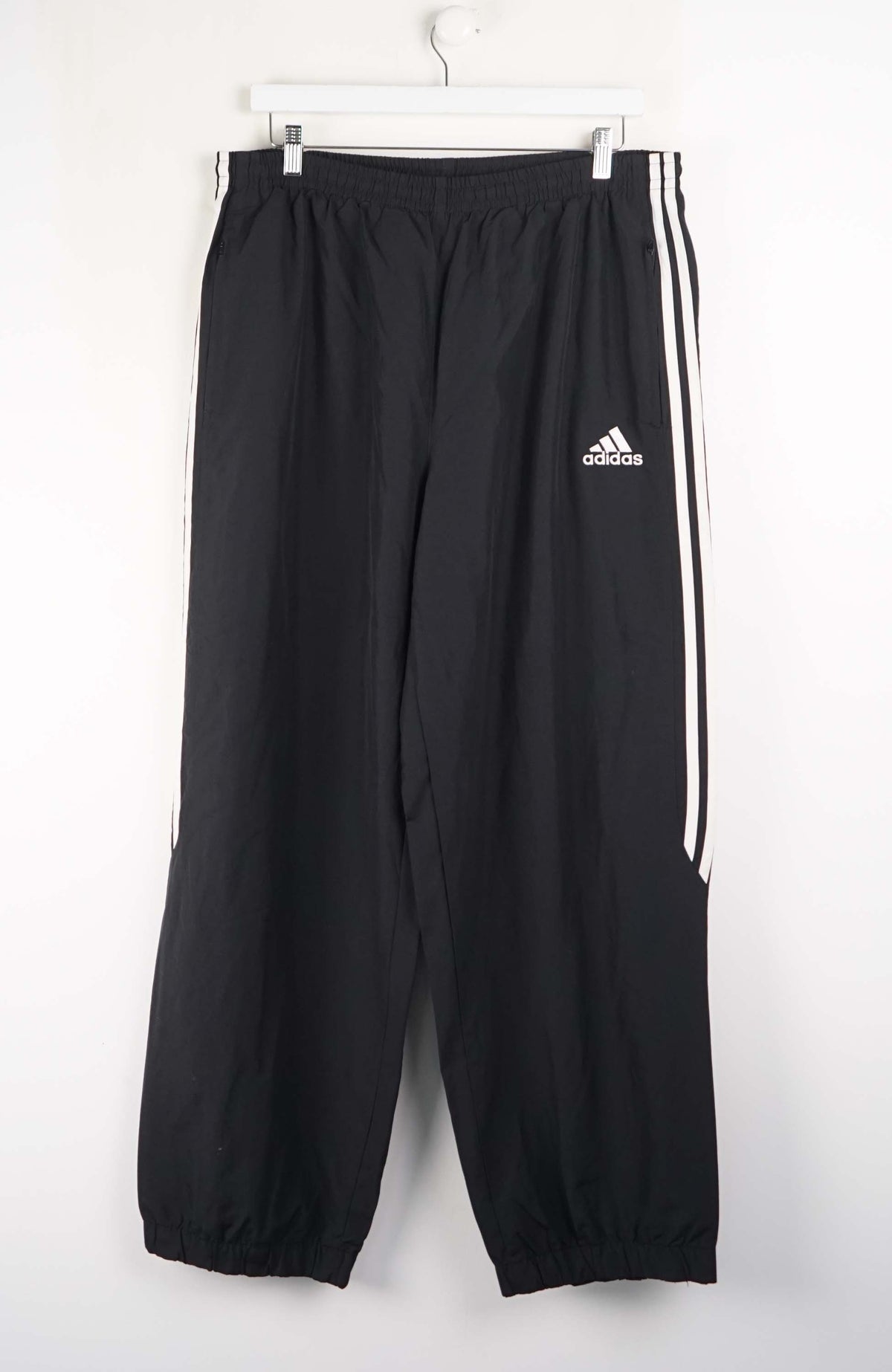 Black Adidas tracksuit pants with white stripes on a white background