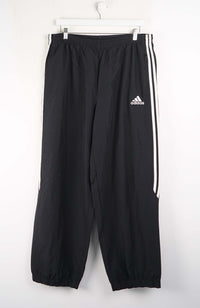 Black Adidas tracksuit pants with white stripes on a white background