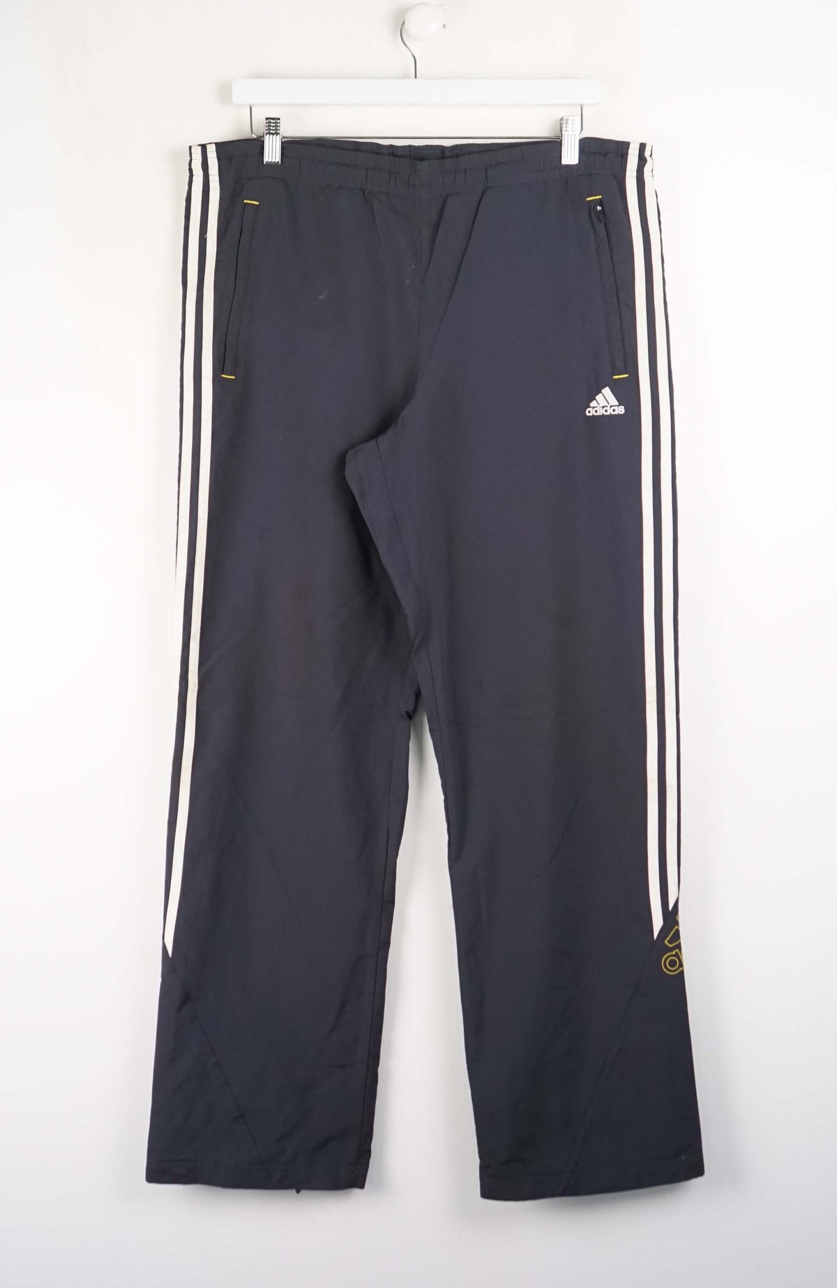 Dark blue Adidas tracksuit pants with white stripes on a white background
