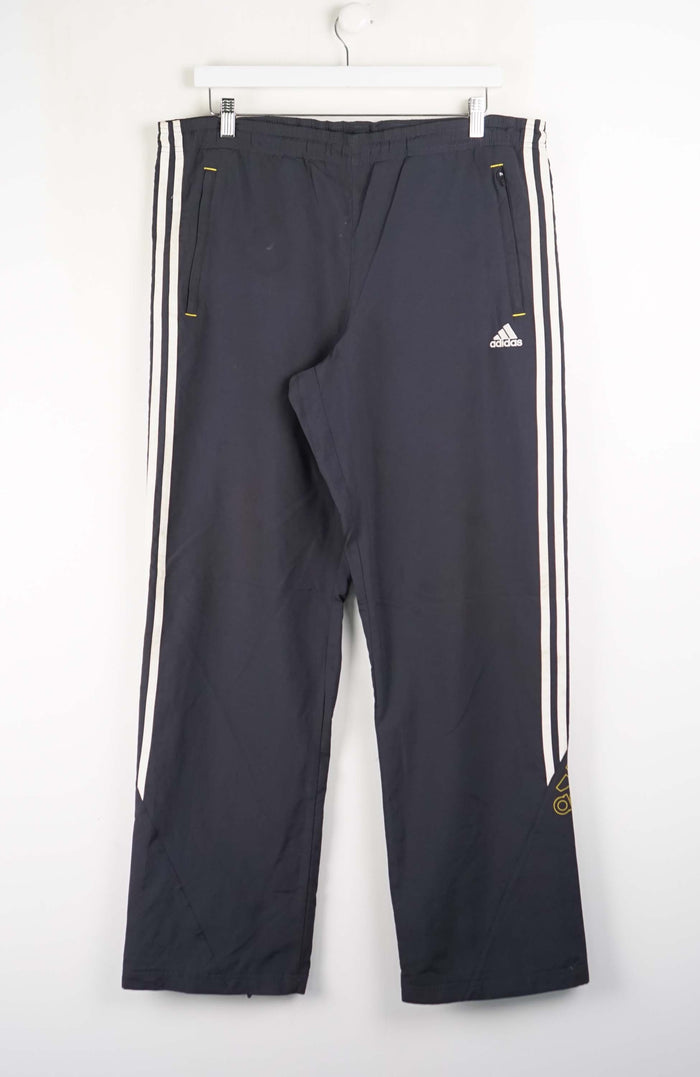 Dark blue Adidas tracksuit pants with white stripes on a white background