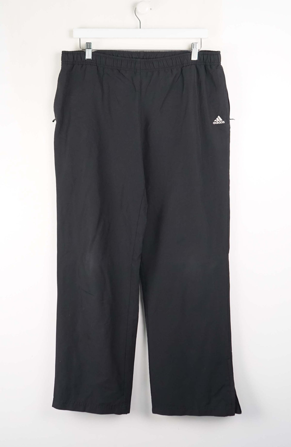 Black Adidas pants hanging on a white background