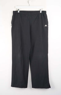 Black Adidas pants hanging on a white background