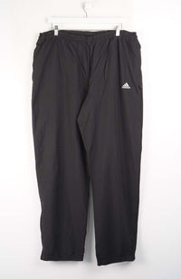 Black Adidas pants hanging on a white background