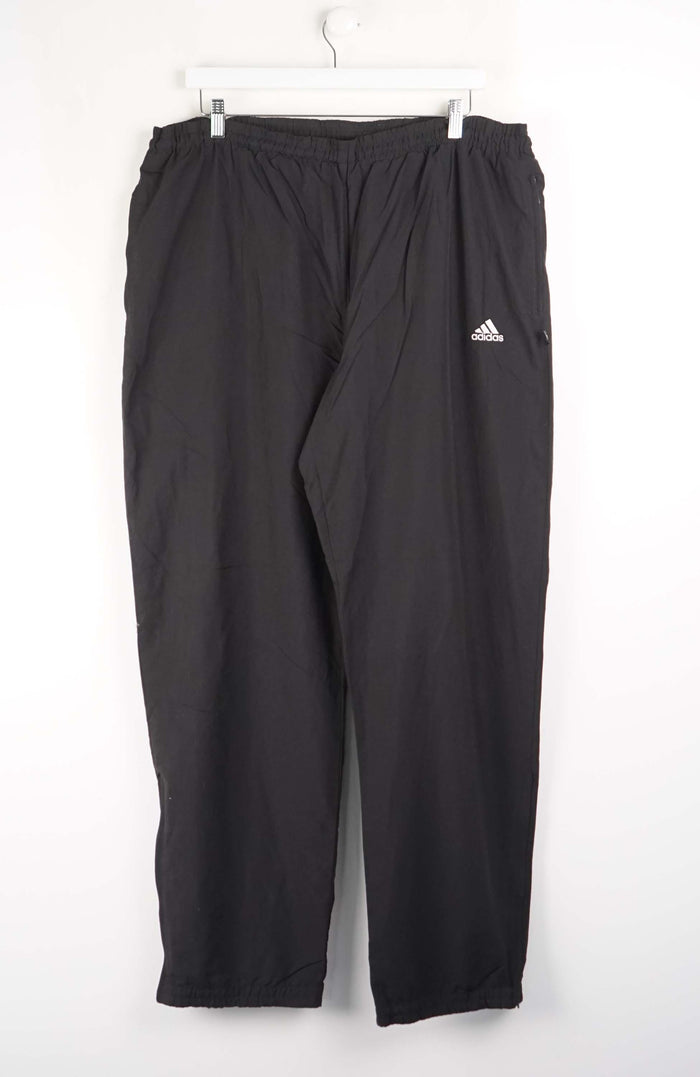 Black Adidas pants hanging on a white background