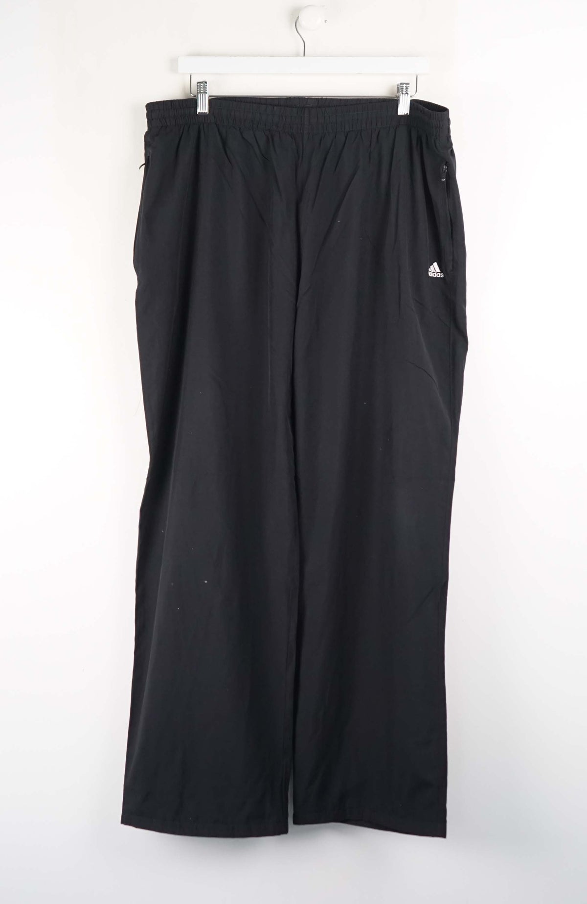 Black Adidas pants hanging on a white background
