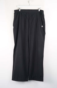 Black Adidas pants hanging on a white background
