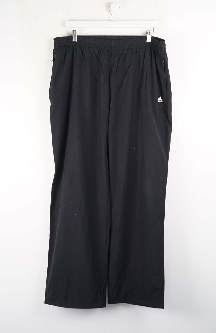 Black Adidas pants hanging on a white background