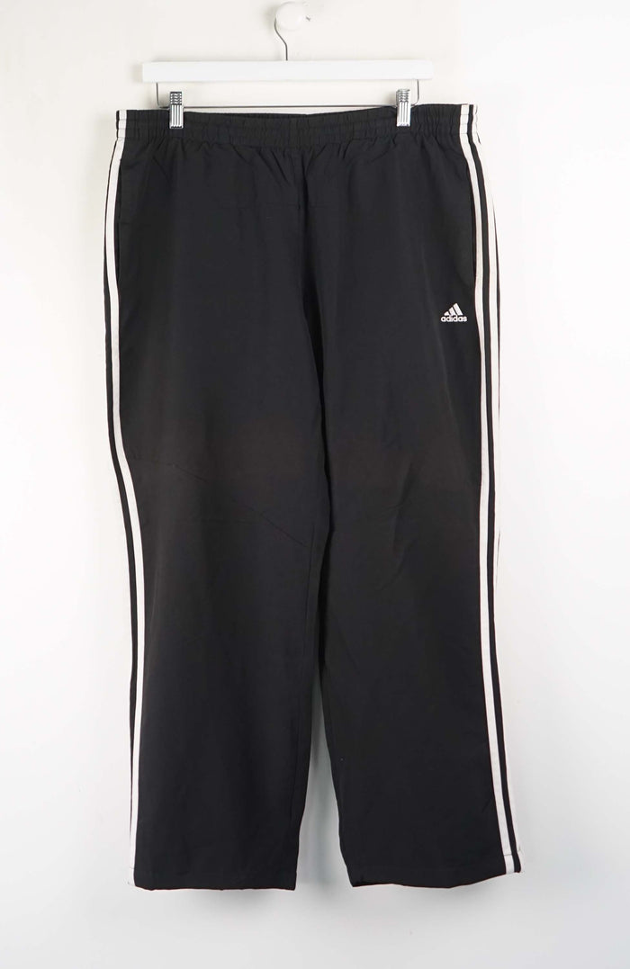 Black Adidas tracksuit pants with white stripes on a white background