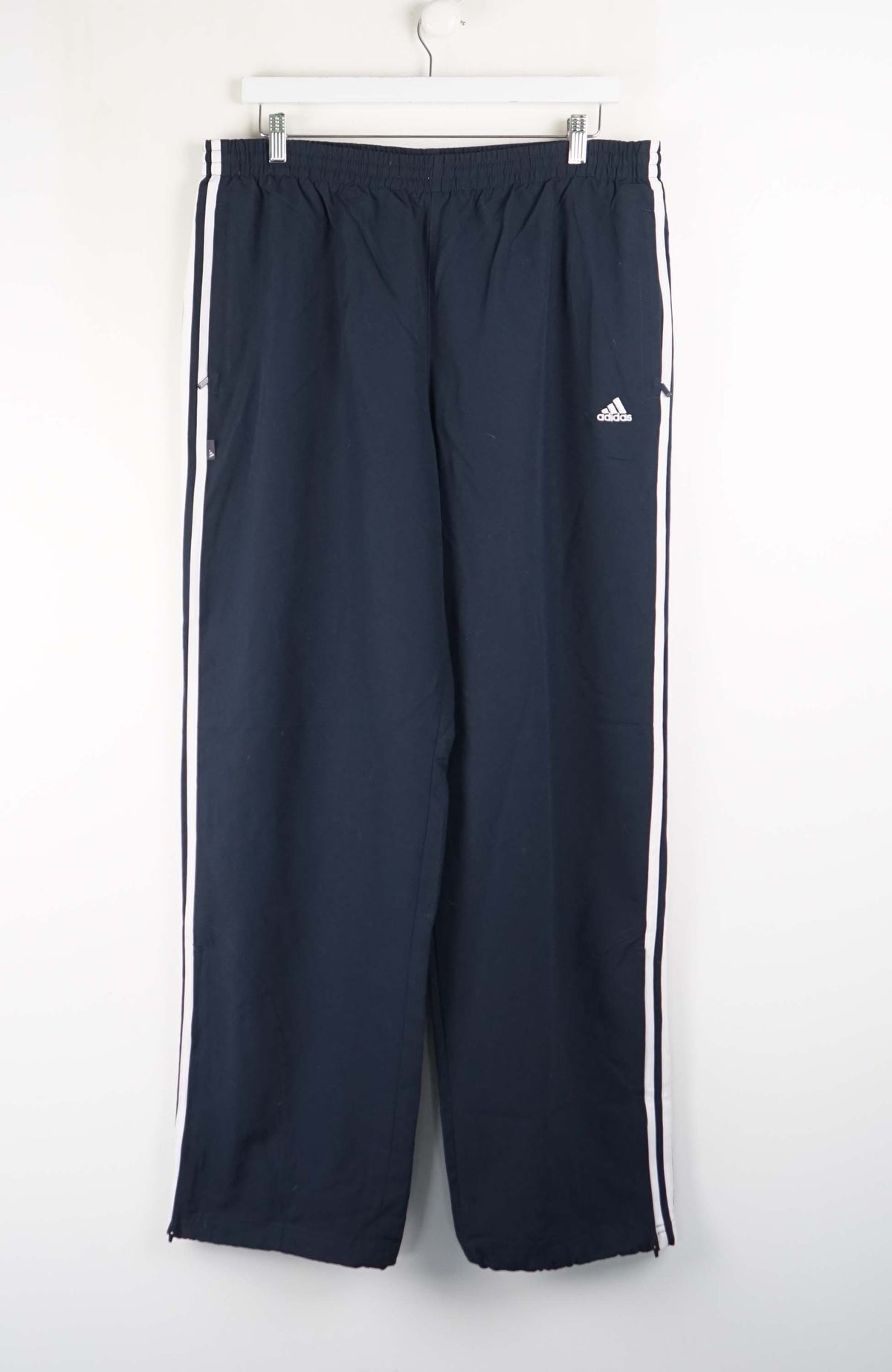 Navy blue Adidas tracksuit pants with white stripes on a white background