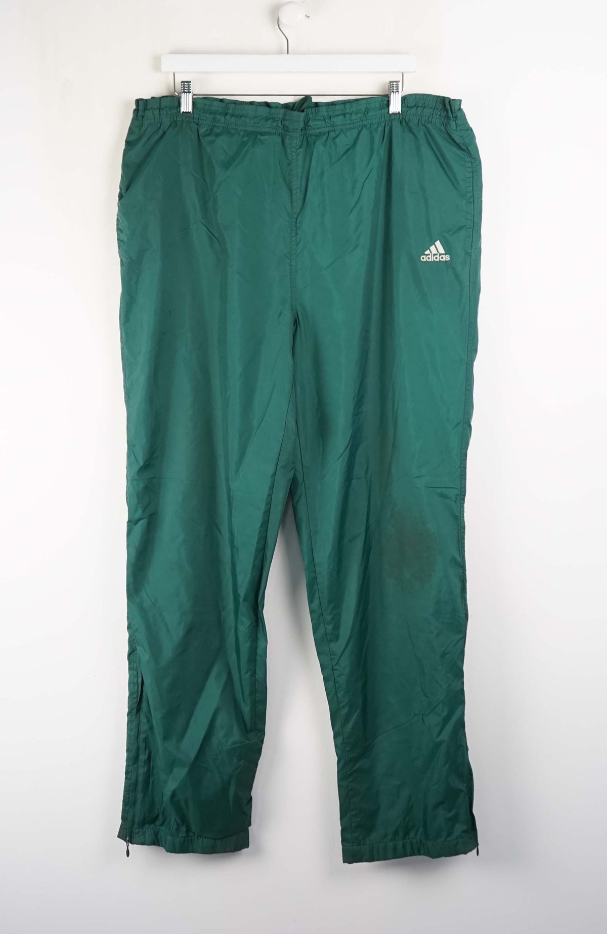 Green Adidas pants hanging on a white background