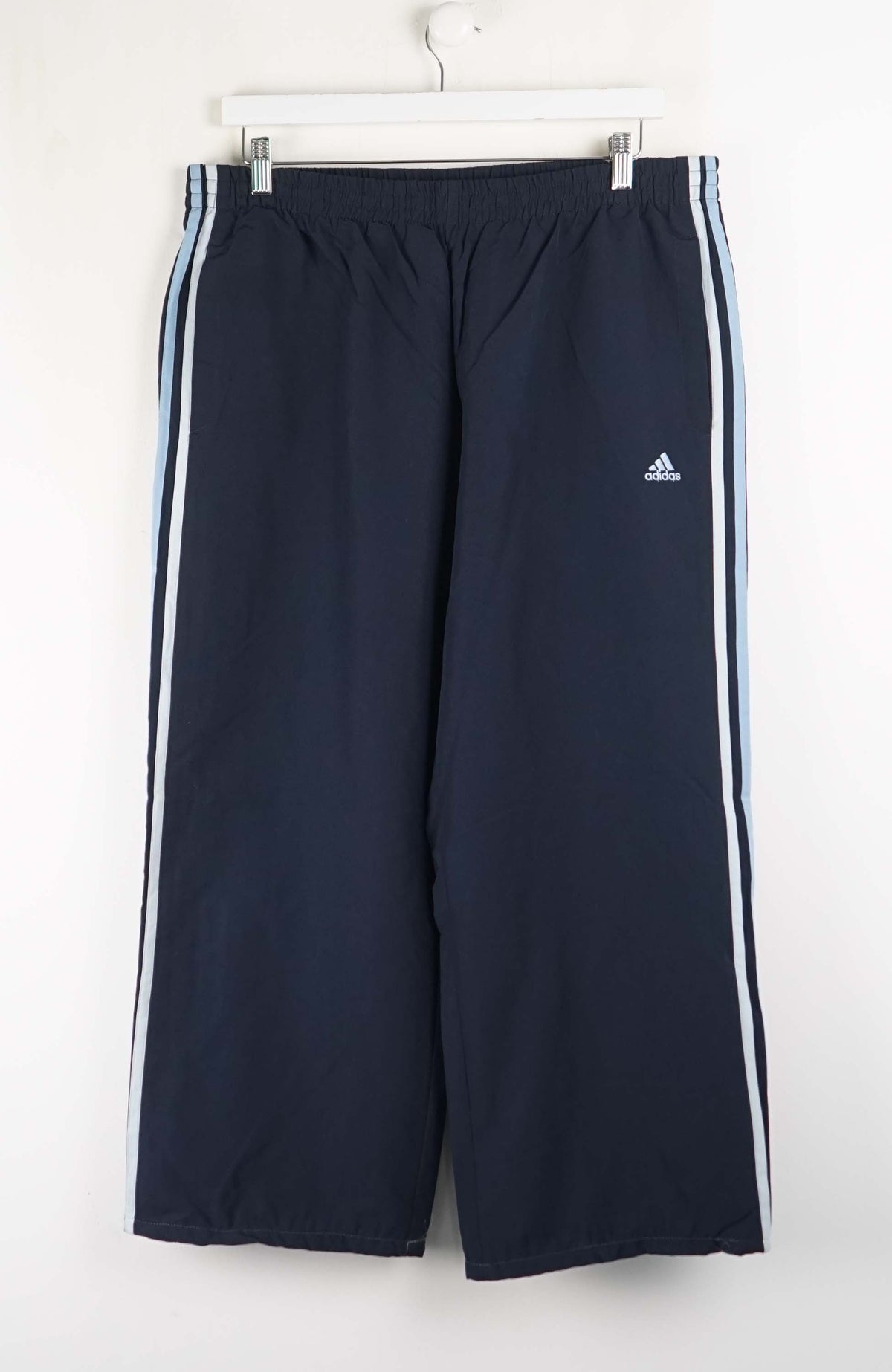 Navy blue Adidas tracksuit pants with white stripes on a white background