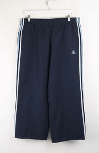 Navy blue Adidas tracksuit pants with white stripes on a white background