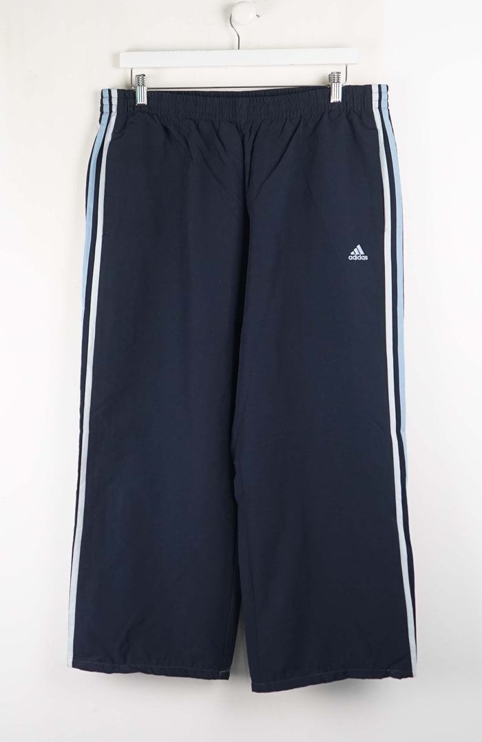 Navy blue Adidas tracksuit pants with white stripes on a white background