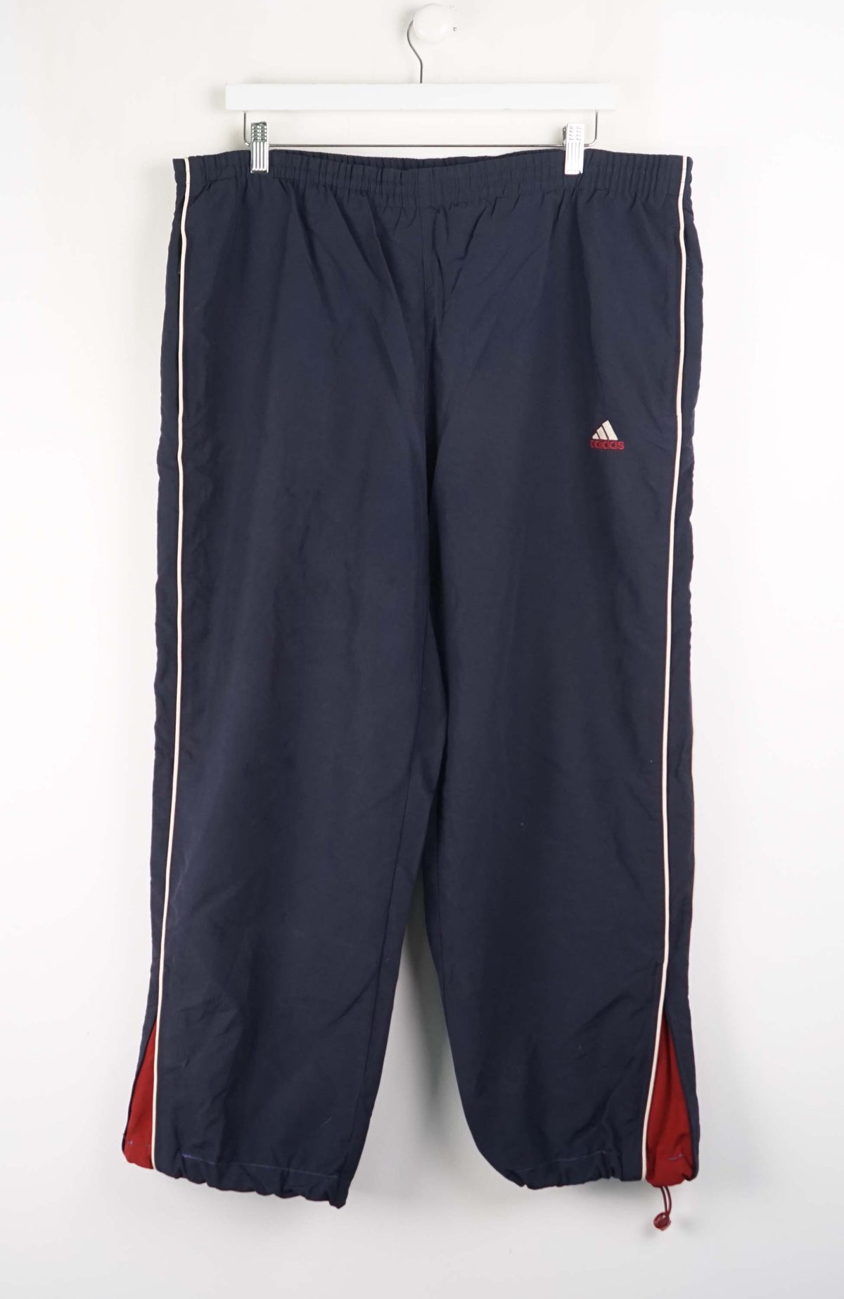 Navy blue tracksuit pants with red and white stripes hanging on a white background