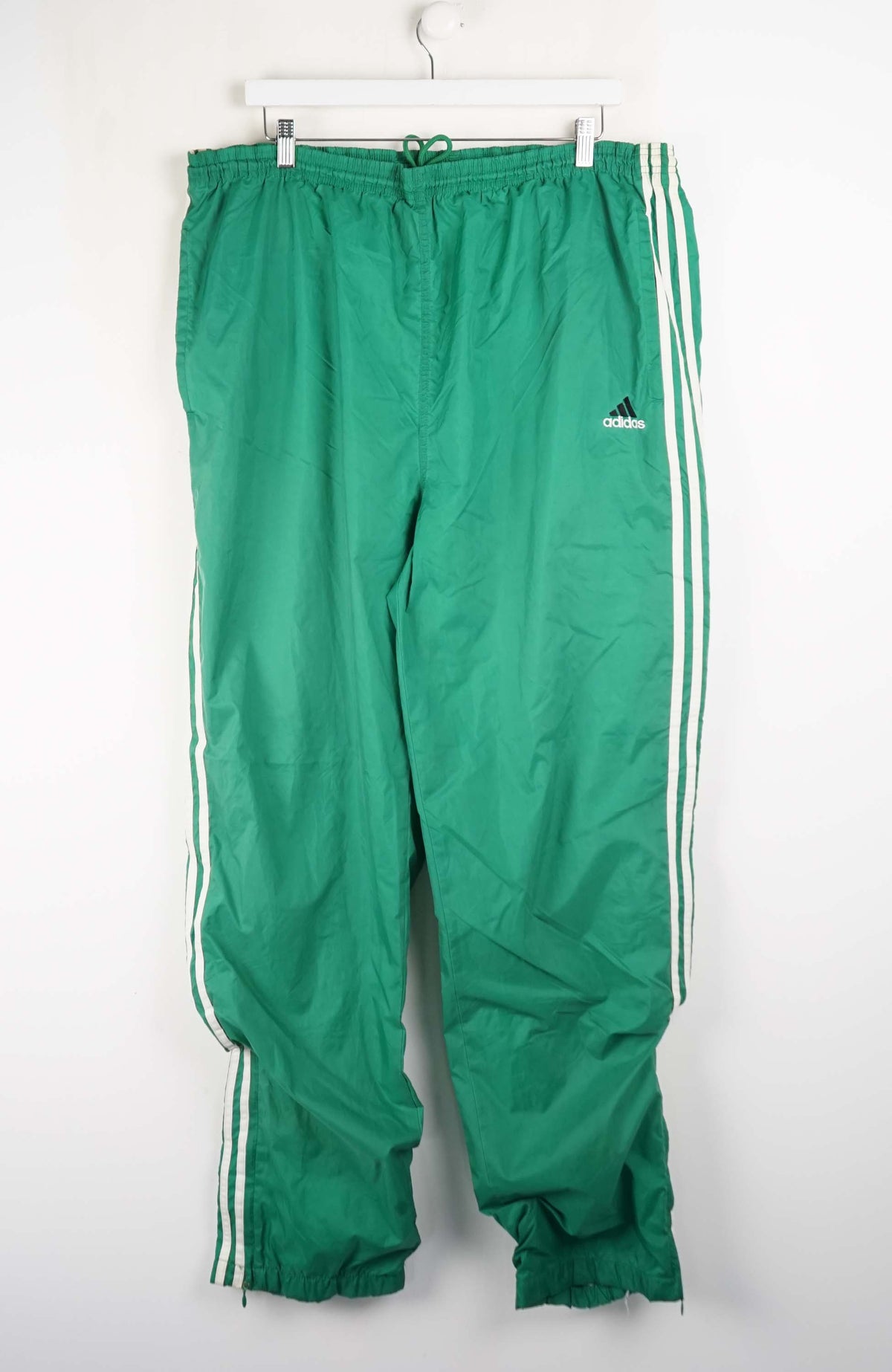 Green Adidas tracksuit pants with white stripes on a white background