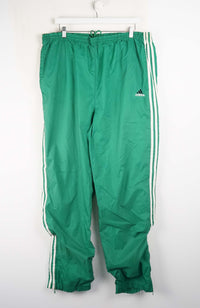 Green Adidas tracksuit pants with white stripes on a white background