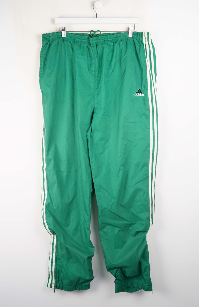 Green Adidas tracksuit pants with white stripes on a white background