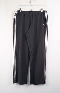 Black Adidas tracksuit pants with three white stripes on a white background