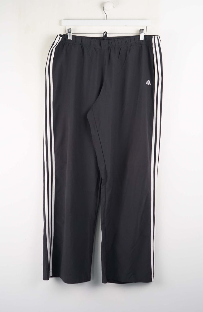 Black Adidas tracksuit pants with three white stripes on a white background