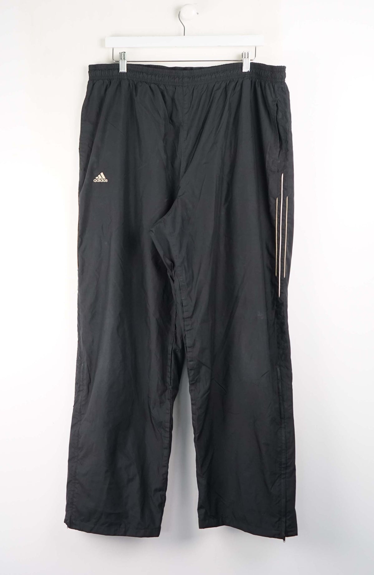 Black Adidas pants hanging on a white background