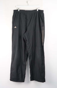 Black Adidas pants hanging on a white background