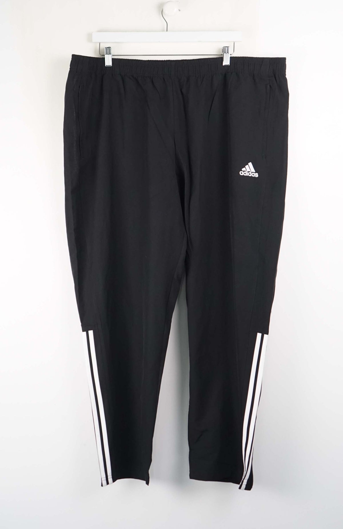 Black Adidas tracksuit pants with white stripes on a white background