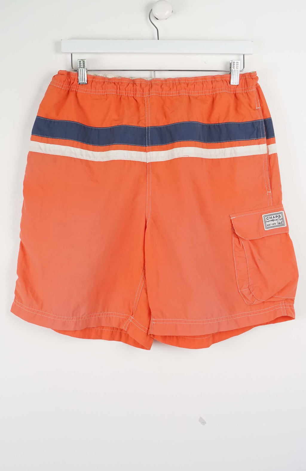 Orange shorts with blue and white stripes hanging on a white background