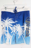 Blue board shorts with palm tree design and brand logo on a white background