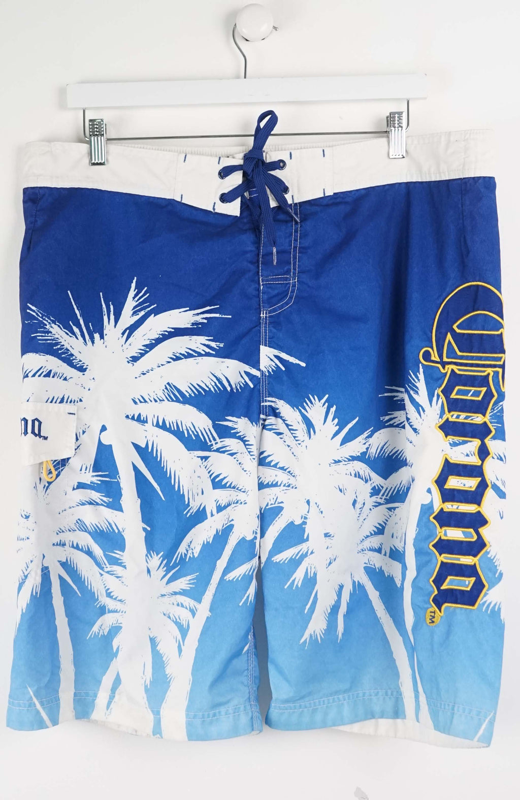 Blue board shorts with palm tree design and brand logo on a white background
