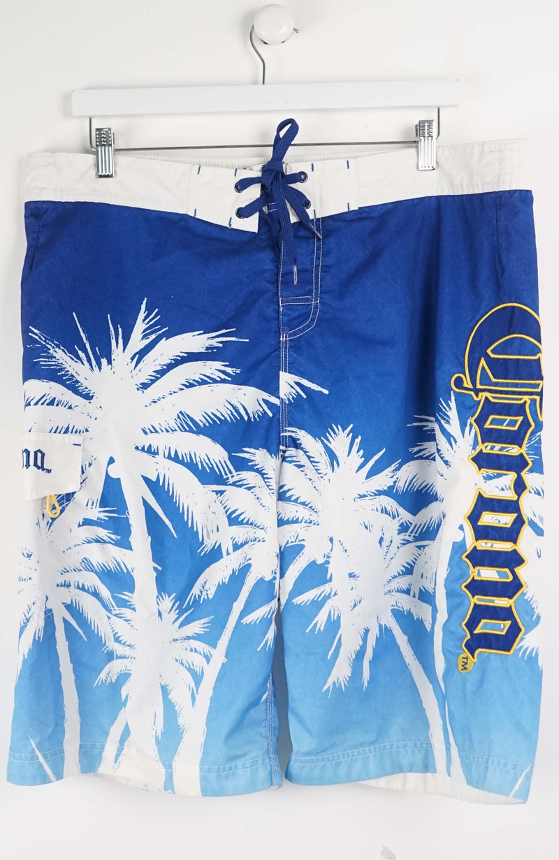 Blue board shorts with palm tree design and brand logo on a white background