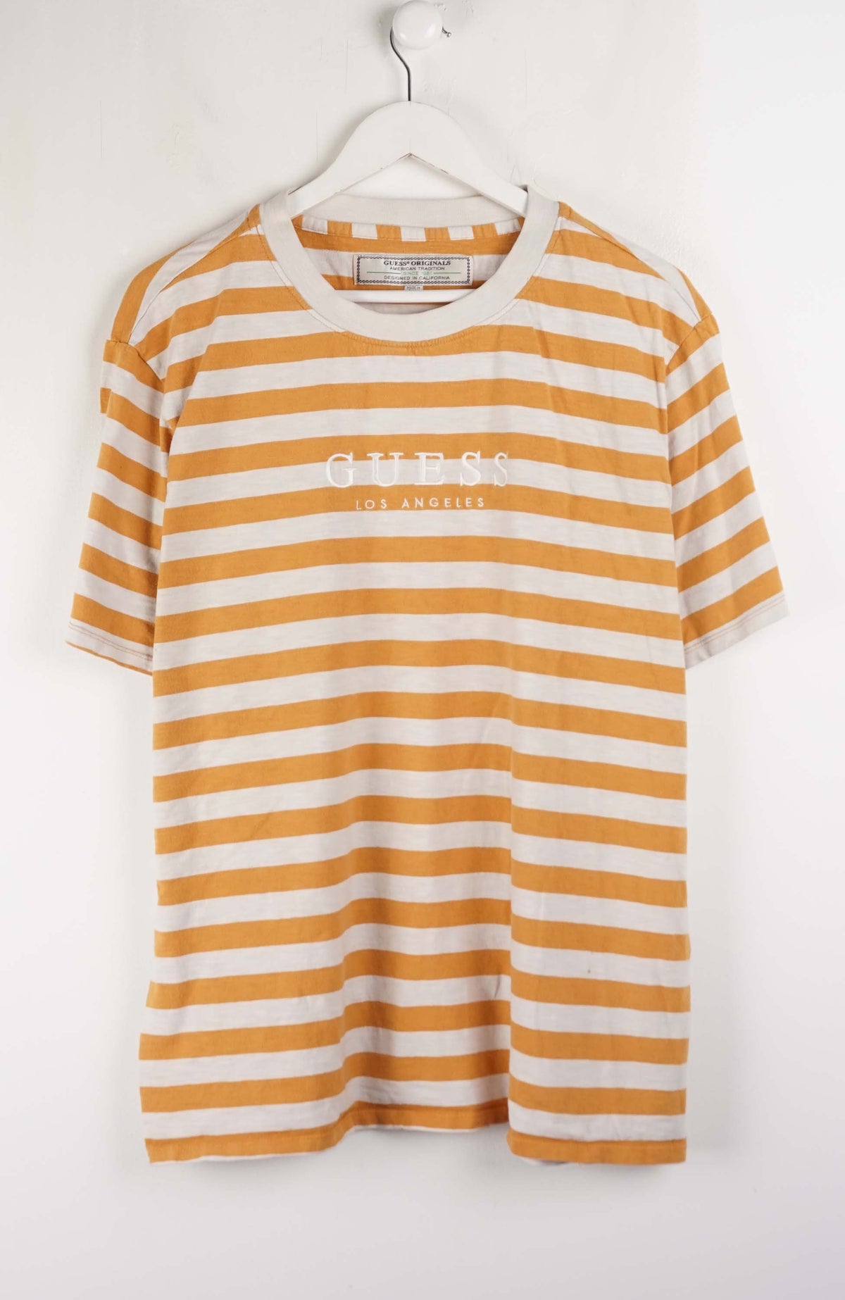 Yellow and white striped t-shirt with 'Guess' logo on a hanger against a white background