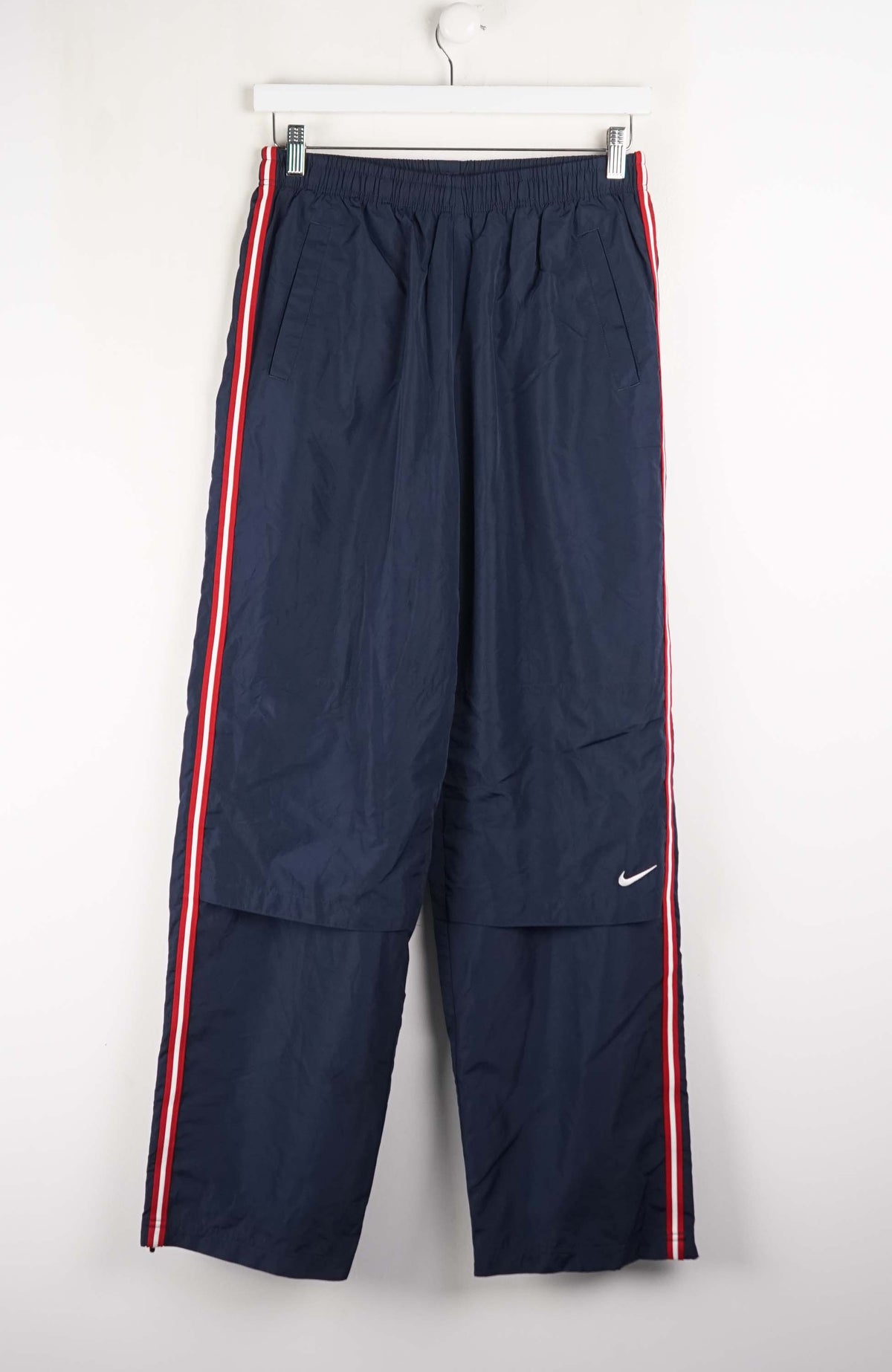Navy blue tracksuit pants with red and white stripes on a white background