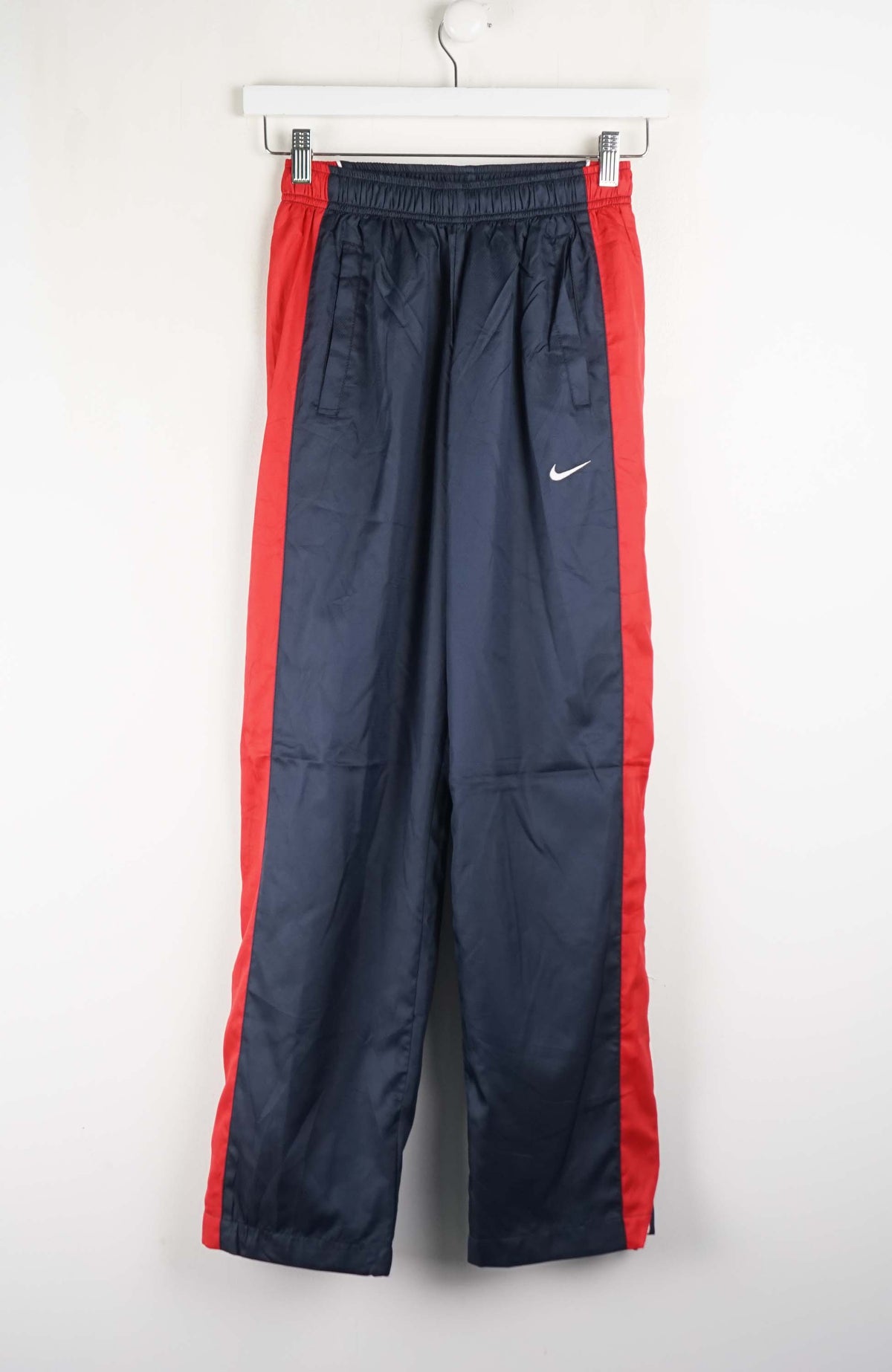 Navy tracksuit pants with red stripes hanging on a white wall.