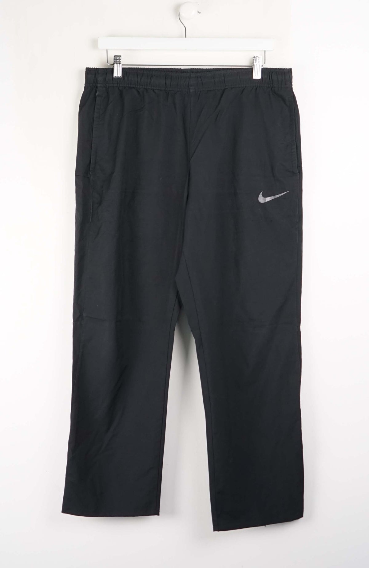 Black Nike pants hanging on a white background