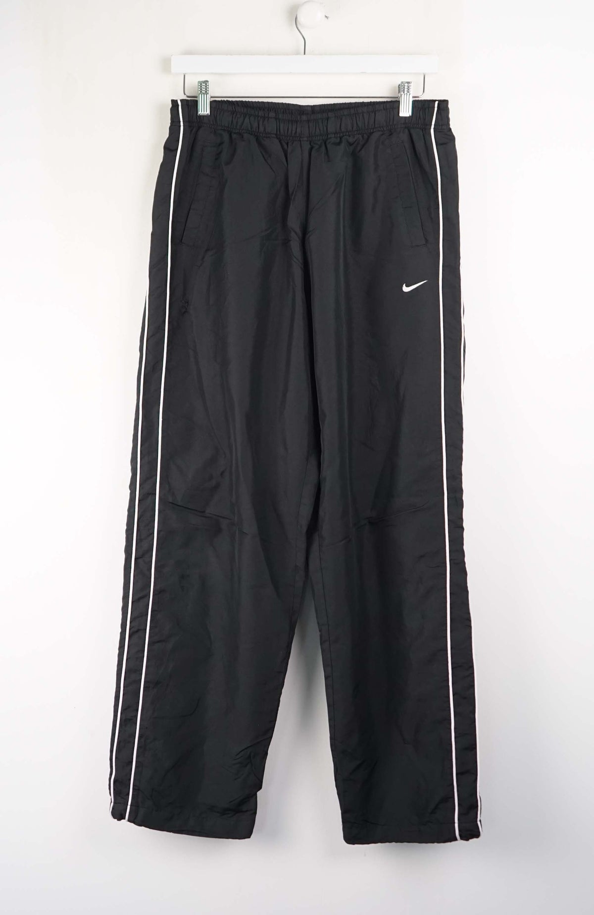 Black track pants with white stripes and Nike logo on a white background