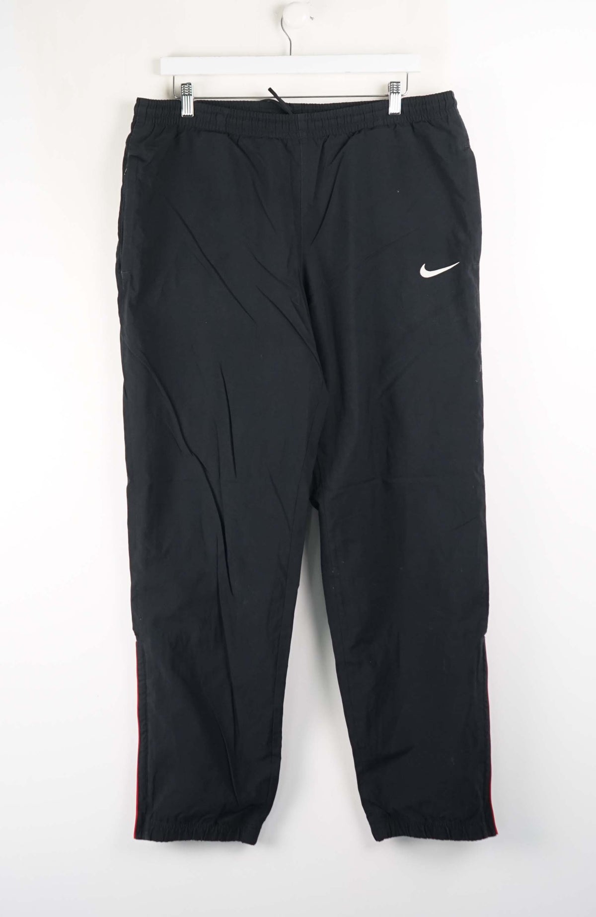 Black Nike pants hanging on a white hanger against a white background