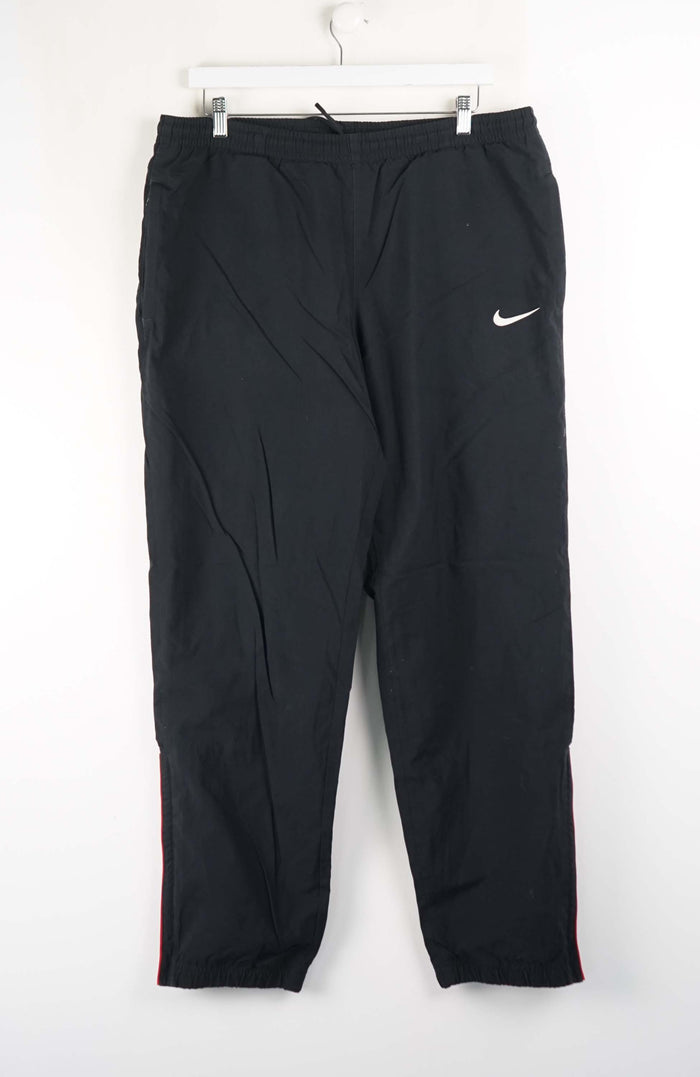 Black Nike pants hanging on a white hanger against a white background