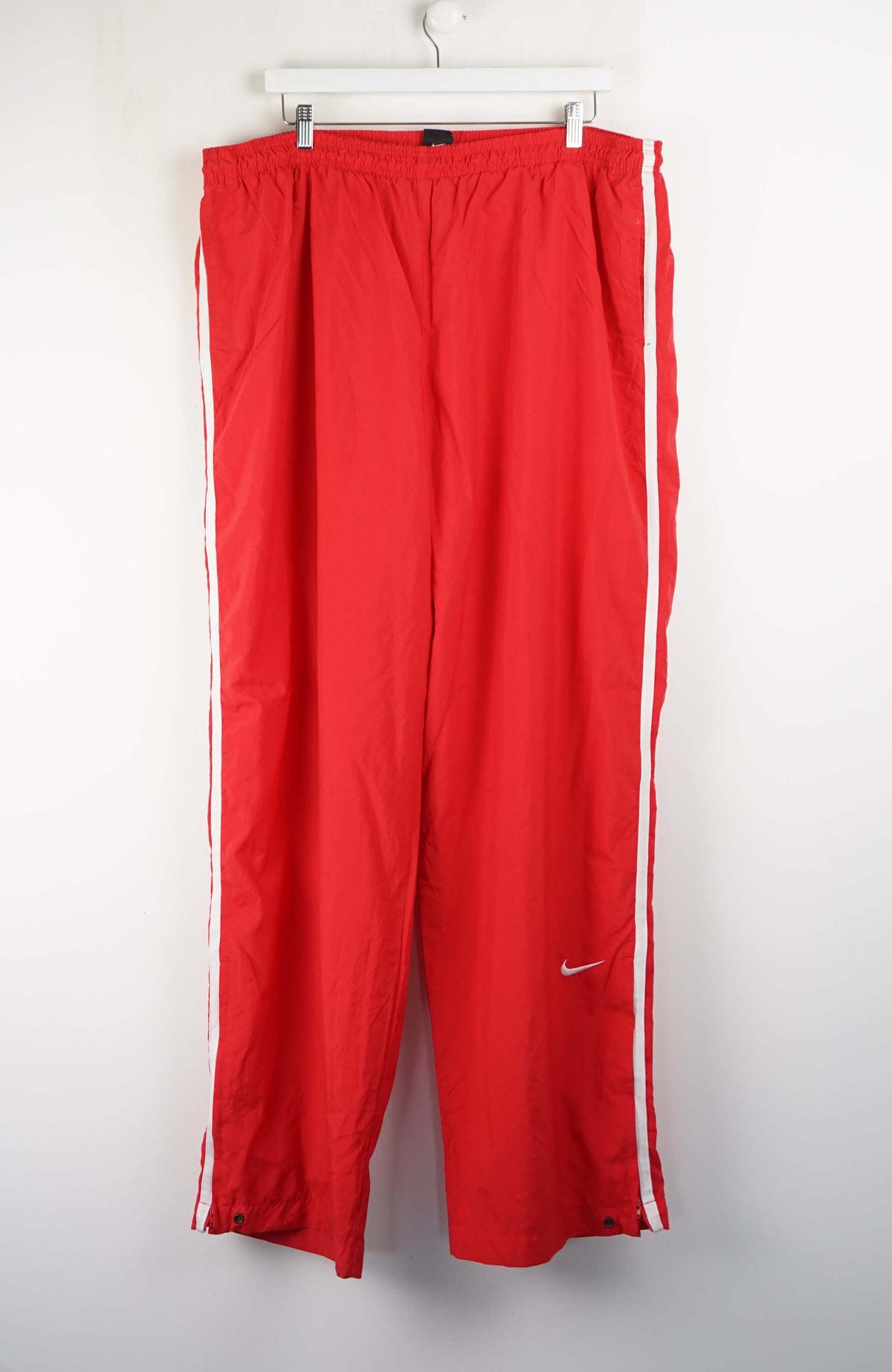 Red track pants with white stripes hanging on a white background