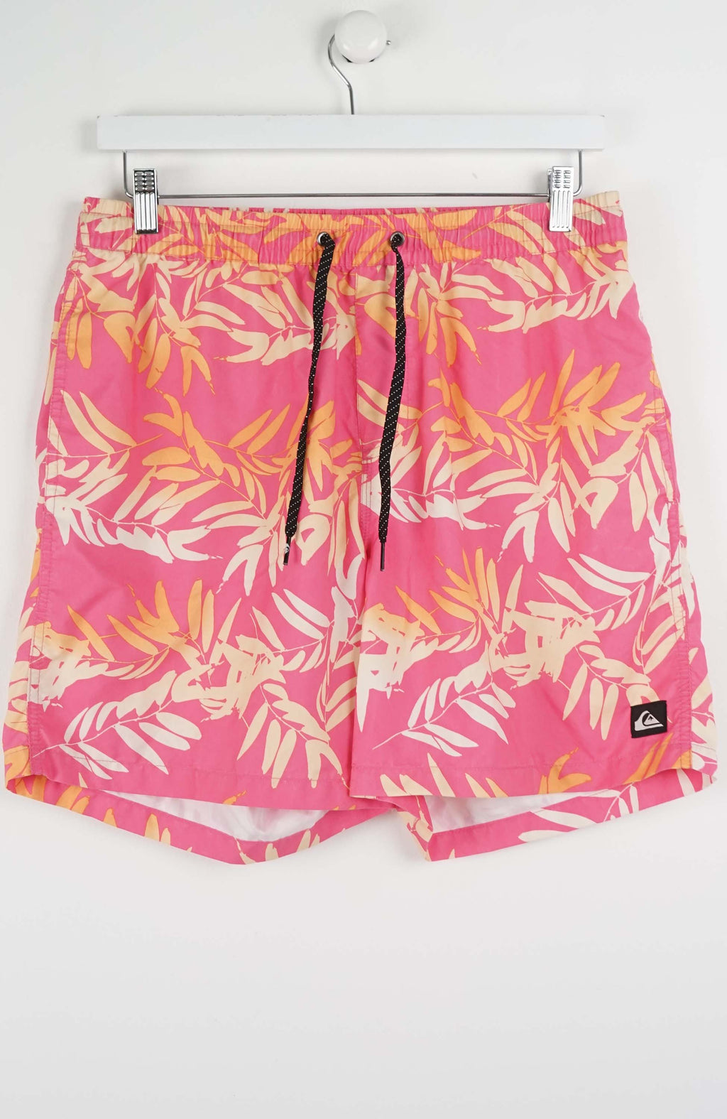 Pink swim shorts with tropical leaf pattern on a white background