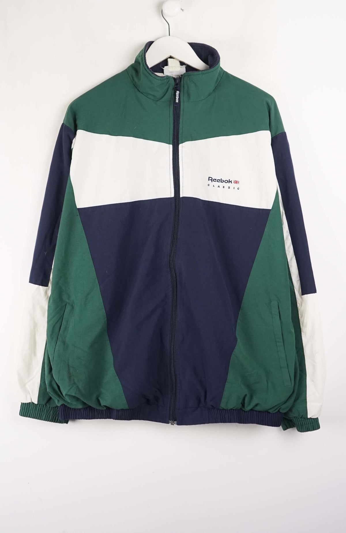 Color-blocked jacket with green, navy, and white sections on a hanger against a white background