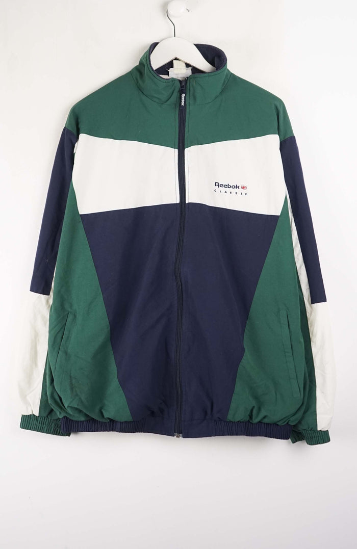 Color-blocked jacket with green, navy, and white sections on a hanger against a white background