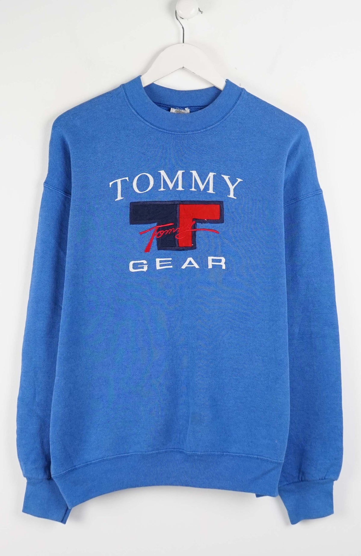 Blue Tommy Gear sweatshirt on a white hanger against a white background