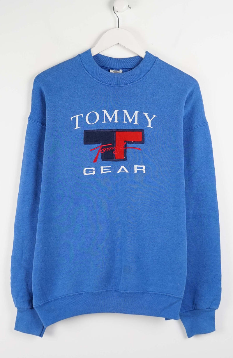 Blue Tommy Gear sweatshirt on a white hanger against a white background