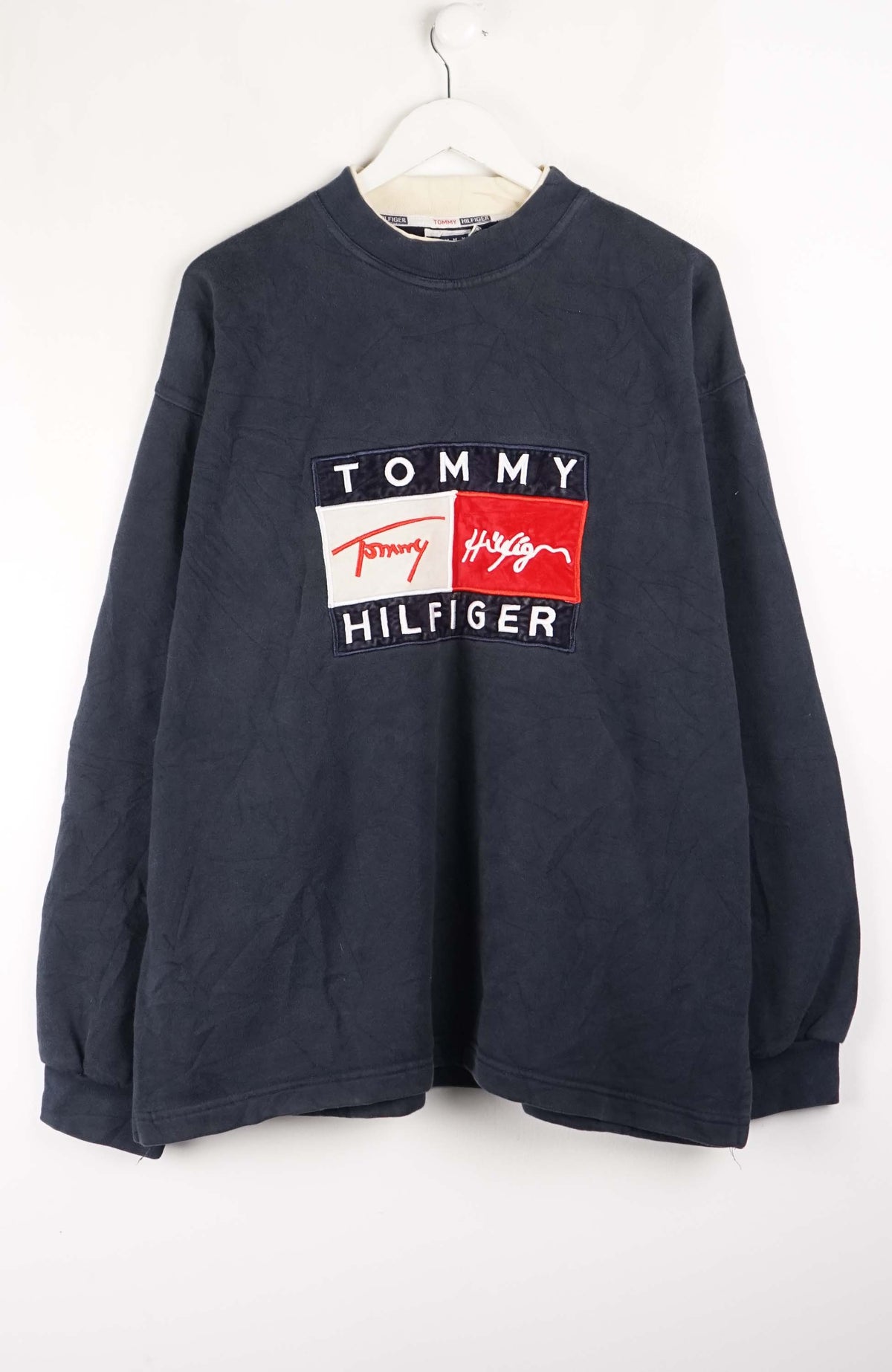 Navy blue Tommy Hilfiger sweatshirt on a white hanger against a white background