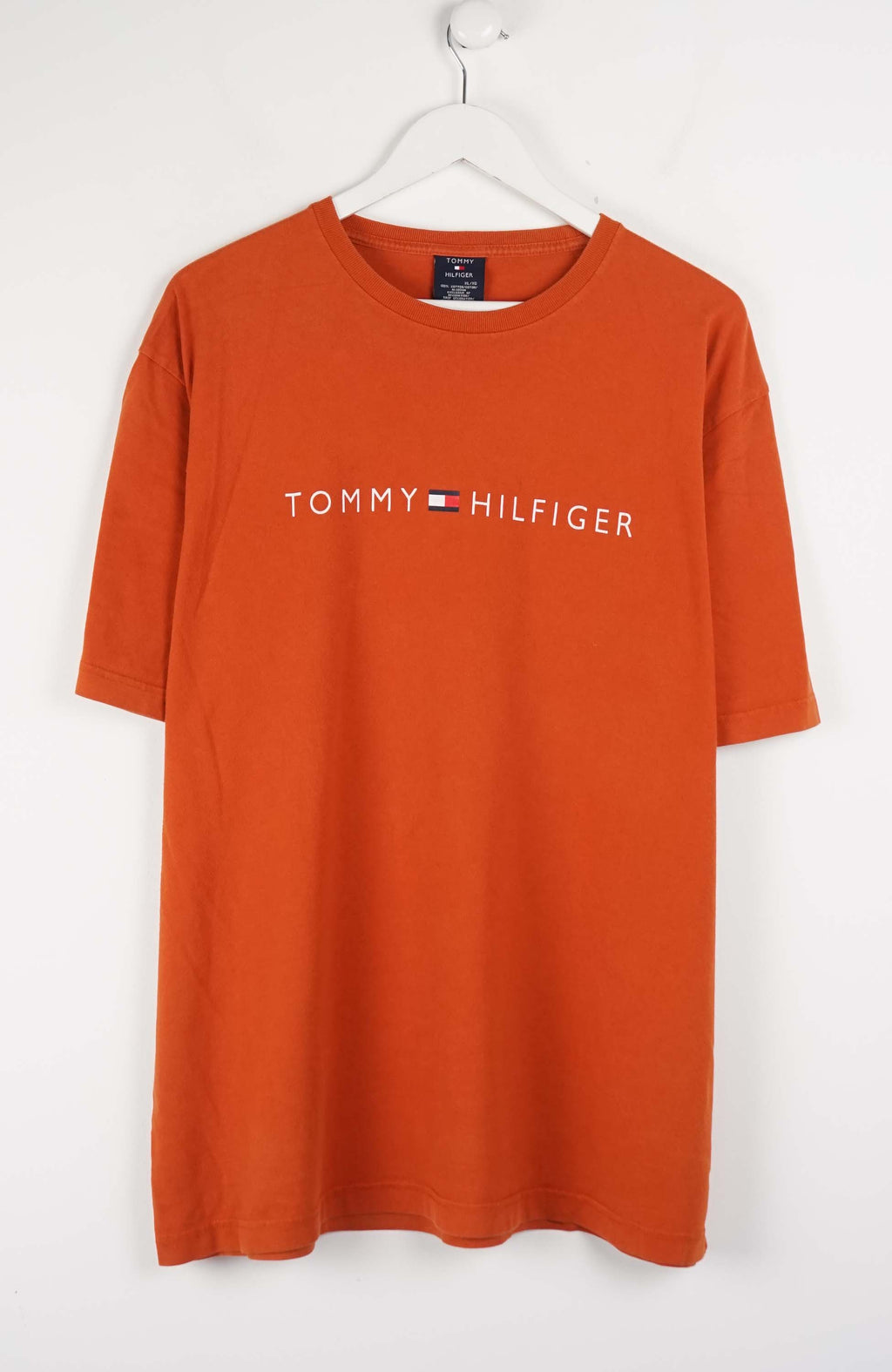 Orange Tommy Hilfiger t-shirt on a white hanger against a white background