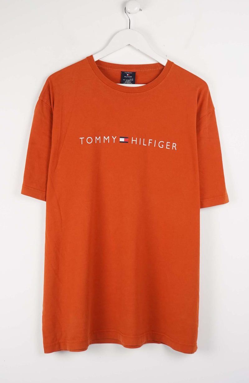 Orange Tommy Hilfiger t-shirt on a white hanger against a white background